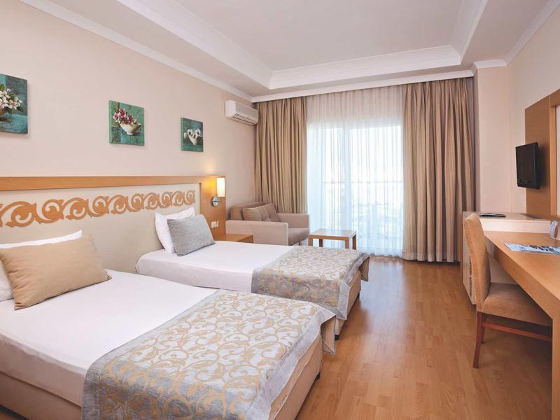 Hell eingerichtetes Hotelzimmer mit zwei Einzelbetten, Schreibtisch, Fernseher und großem Fenster.