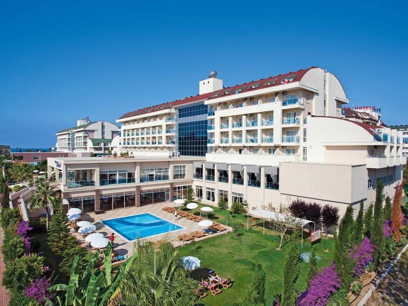 Großes Hotelgebäude mit mehreren Etagen, Pool im Garten und grünem Rasen bei klarem Himmel.