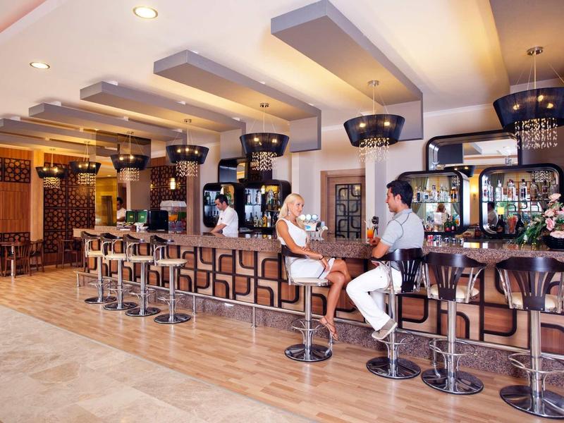 Moderner Barbereich mit beleuchtetem Tresen, hohen Hockern und drei Personen in heller, stilvoller Einrichtung.