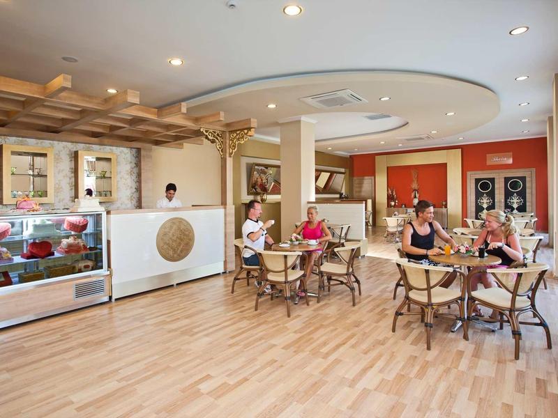 Ein heller, moderner Cafébereich mit hölzernem Boden, Tischen, Stühlen und Gästen, die sich unterhalten.