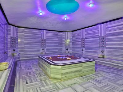 Moderner Whirlpool in einem Raum mit grauen, gestreiften Wand- und Bodenfliesen und blauer Deckenbeleuchtung.