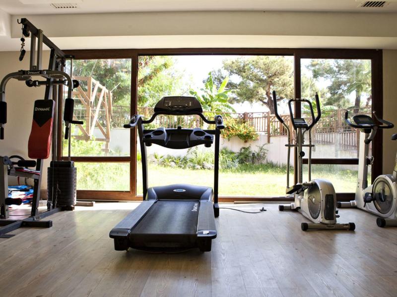 Světle vybavená posilovna se stroji a výhledem na zahradu.