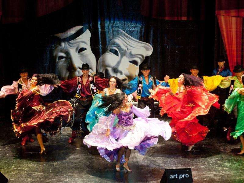 Barevné folklorní tanečnice točící se na jevišti před černými závěsy.