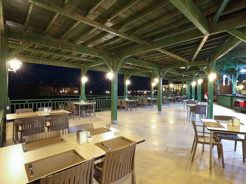 Zastřešená terasa restaurace se dřevěným nábytkem a výhledem na tmavé venkovní prostředí v noci.