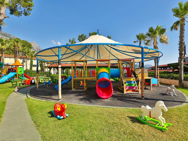 Barevné dětské hřiště s klouzačkami a houpačkami na zelené trávě pod modrou oblohou