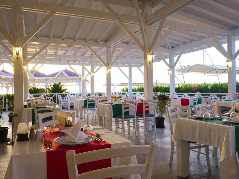 Otevřená restaurace s prostřenými stoly, bílými židlemi a slunečníky v pozadí.