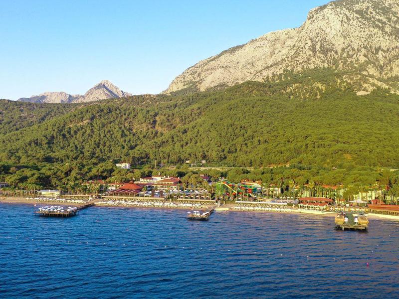 Pobřeží s pláží, loděmi a kopci v pozadí za jasné oblohy.