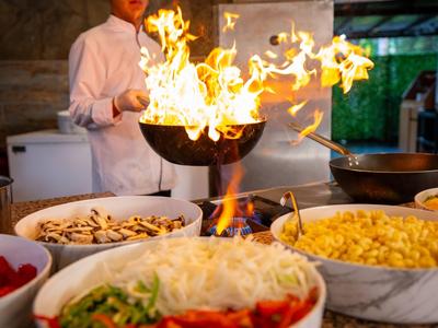 Koch wendet Flammen in einer Pfanne in einer Küche mit frischen Zutaten auf dem Tisch.
