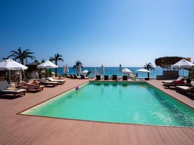 Poolbereich mit Sonnenliegen und Schirmen am Meer bei klarem Himmel