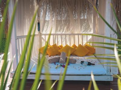 Entspannte Person liegt auf einem weißem Outdoor-Bett mit orangen Kissen unter einem strohgedeckten Pavillon.