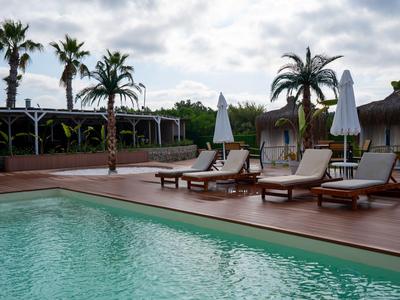 Poolbereich mit Liegestühlen, Sonnenschirmen und Palmen unter bewölktem Himmel.