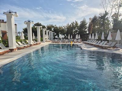 Großer Außenpool mit Liegestühlen und Sonnenschirmen an einem sonnigen Tag.