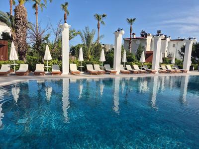 Klare blaue Poolwasser mit Liegestühlen und weißen Sonnenschirmen im Hotelgarten.