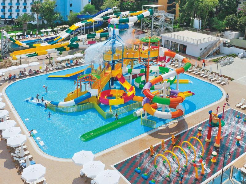 Barevný vodní park s mnoha skluzavkami, bazény a herními oblastmi obklopený lehátky.