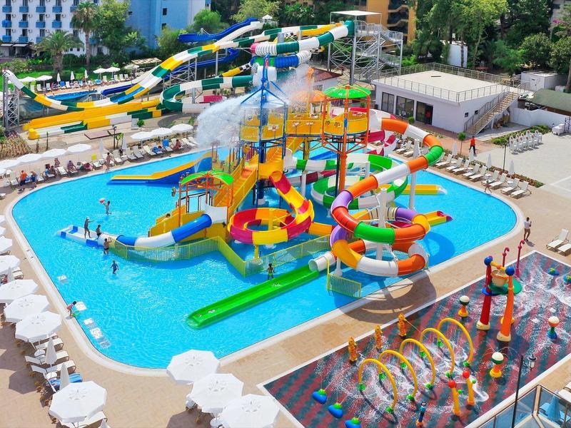 Barevný bazén aquaparku s skluzavkami, vodními atrakcemi a lehátky v hotelové oblasti.