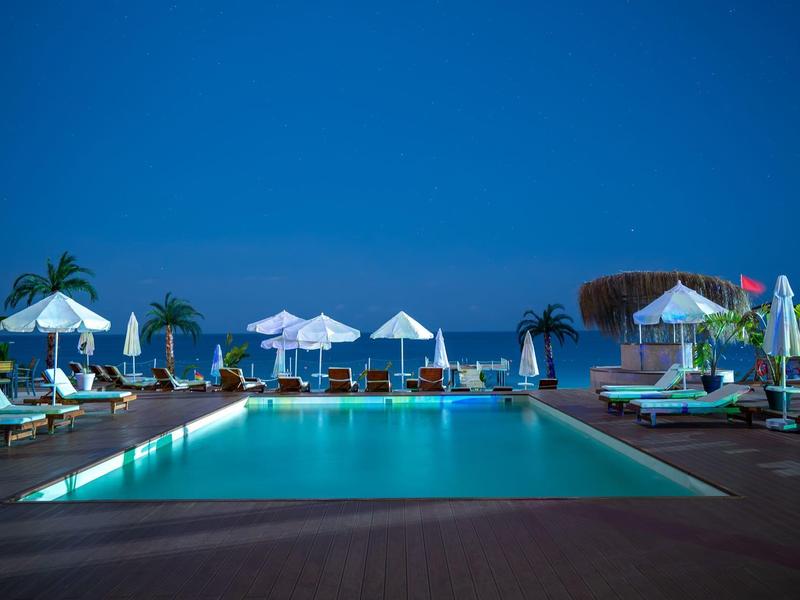 Osvětlená bazénová část s lehátky a slunečníky večer