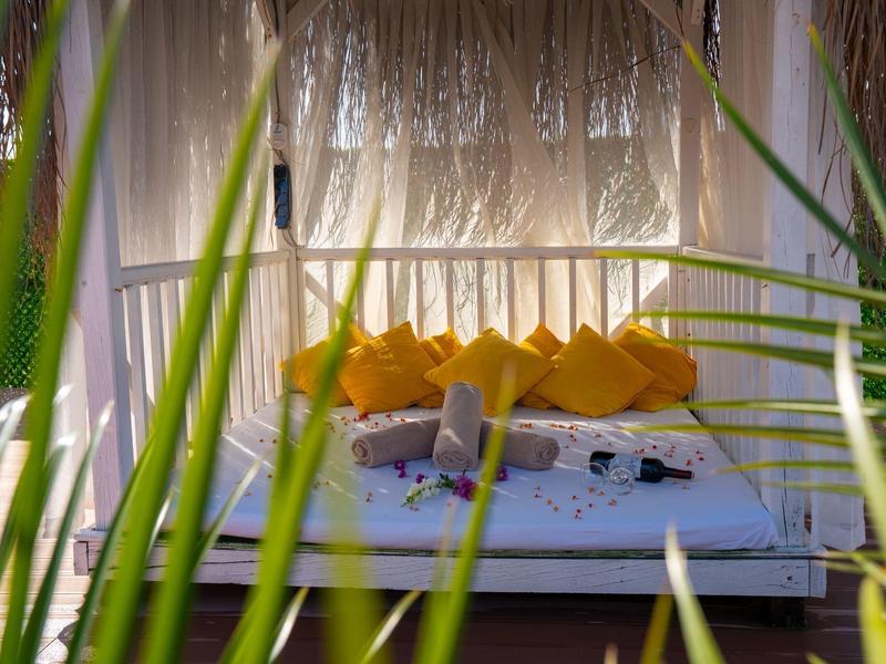 Pohodlný lounge prostor s bílými pohovkami a žlutými polštáři, obklopený zelenými rostlinami.