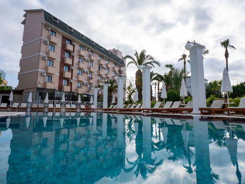 Moderní hotelový komplex s bazénem, palmami a slunečníky pod zataženou oblohou.