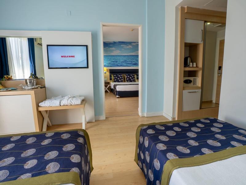 Hotelový pokoj se dvěma jednolůžky, televizí na zdi a výhledem do sousedního pokoje.