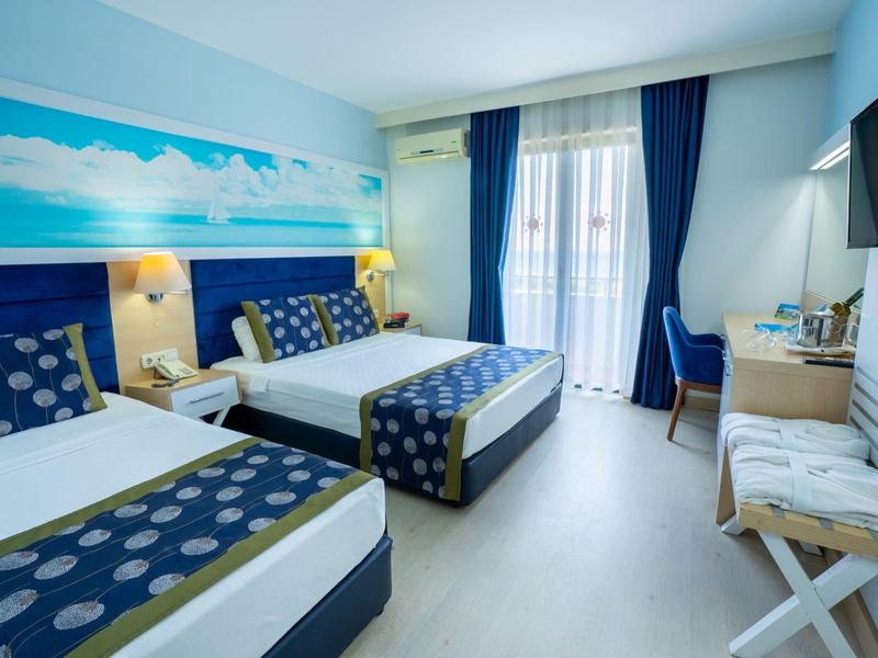 Hotelový pokoj se dvěma manželskými postelemi, modrými závěsy a námořnickou výzdobou na stěně.