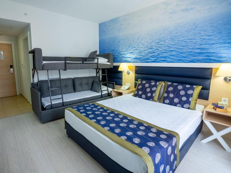 Hotelový pokoj s manželskou postelí, palandou, dřevěnou podlahou a nástěnnou malbou oceánu.