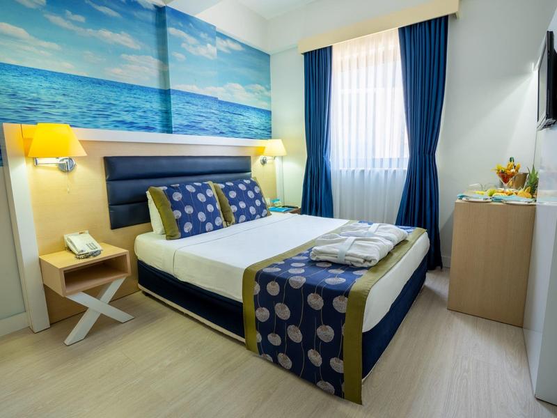 Moderní hotelový pokoj s manželskou postelí, námořnickým dekorací a světlým dřevěným nábytkem.