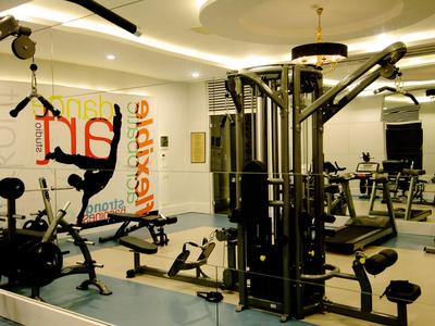 Modernes Fitnessstudio mit Kraftgeräten, Spiegelwand, Hantelbänken und hellem Deckenlicht.