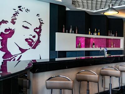 Moderner Barbereich mit beige Stühlen, schwarzer Theke und großer Marilyn-Monroe-Wandkunst in Pink und Weiß.