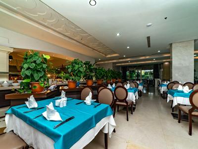 Großer Restaurantraum mit blauen Tischdecken, weißen Servietten und braunen Stühlen, Pflanzen als Dekor.