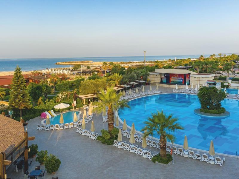Grande piscina rotonda con ombrelloni e palme accanto a un hotel vicino al mare