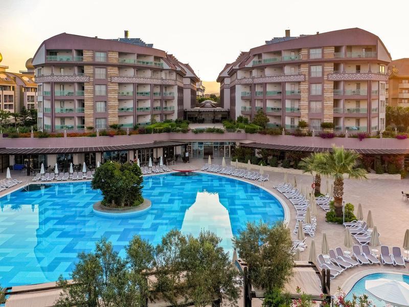 Grande hotel con due edifici e una grande piscina con lettini al tramonto.