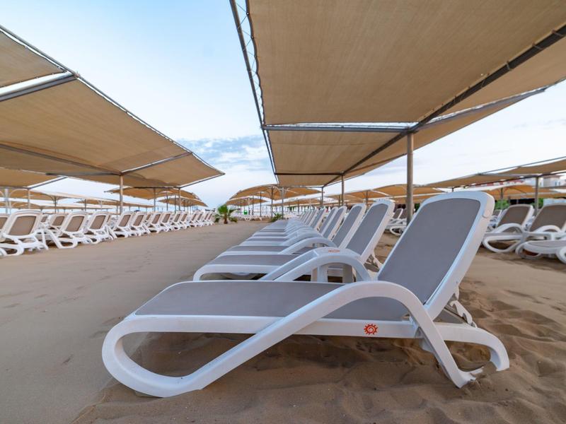 Lettini vuoti con tende ombreggianti su spiaggia sabbiosa sotto cielo azzurro.