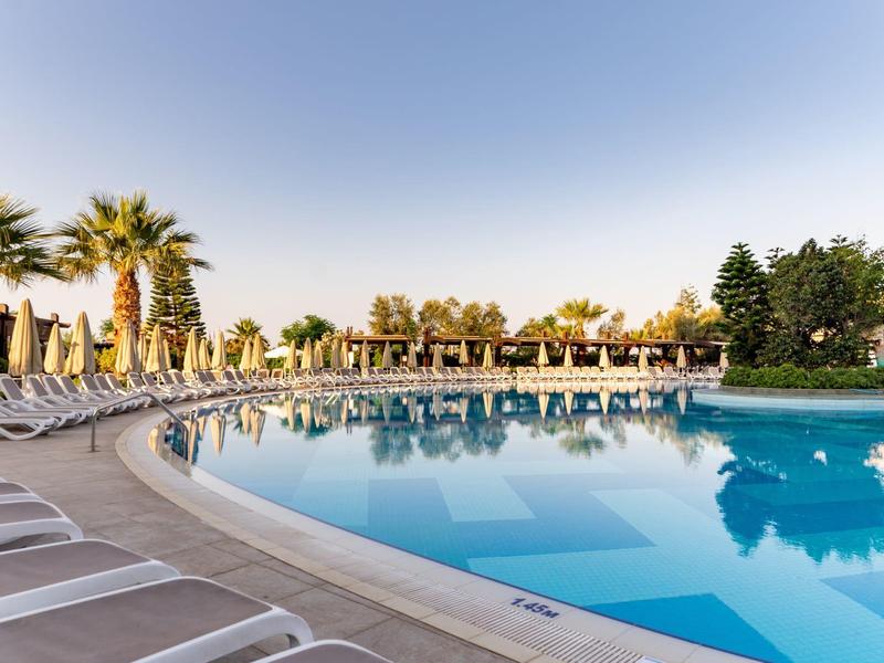 Grande piscina dell'hotel con lettini e ombrelloni sotto un cielo azzurro.