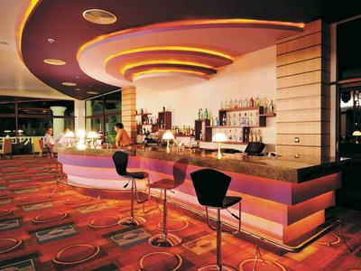 Moderne Bar mit geschwungenem Tresen, bunter Beleuchtung und roten Teppichboden mit Muster.