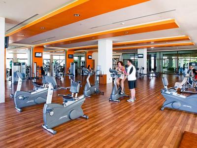 Großer Fitnessraum mit Holzfußboden, mehreren Cardiogeräten und orangefarbenen Deckenstreifen.