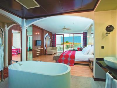 Helles Hotelzimmer mit offenem Bad, Doppelbett, Balkon und Meerblick, moderne Holzmöbel.