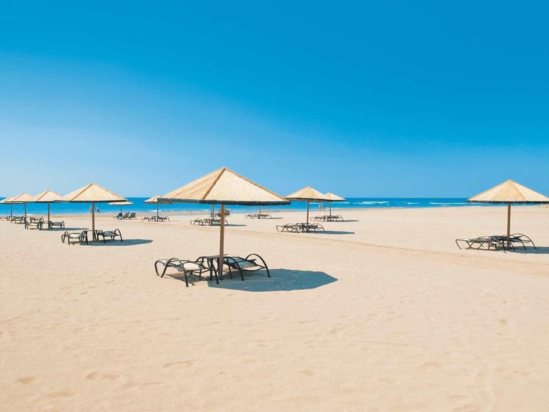 Expansive sandy beach with sun umbrellas and lounge chairs under a clear blue sky.