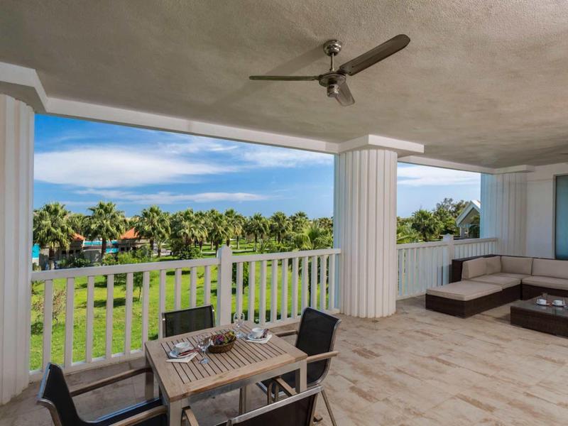 Spacious terrace with dining table, chairs, ceiling fan, and view of green palm trees.