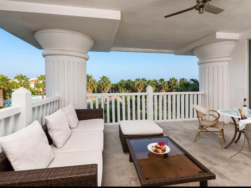 Terrace with seating area and dining table, overlooking palm trees and blue sky.