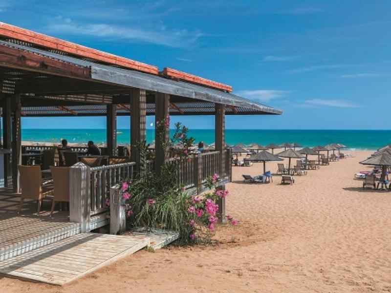 Open beach café overlooking sun loungers and the blue sea under a clear sky.