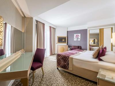 Modernes Hotelzimmer mit Doppelbett, violetten Akzenten, Schreibtisch, Stuhl und Teppichboden.