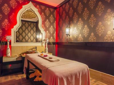 Behandlungsraum mit Massageliege, orientalischer Wanddekoration und warmem Lichtambiente.