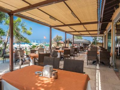 Offenes Restaurant am Strand mit Tischen, Stühlen und Sonnenschirmen bei blauem Himmel.