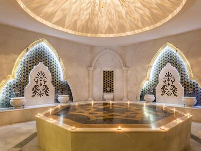 Helles Hammam mit zentralem Marmorbecken, geschnitzten Wandnischen und warmem indirektem Licht.
