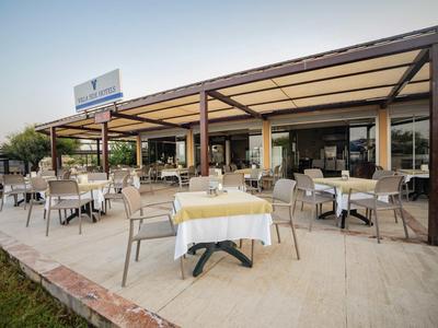 Große Terrasse eines Restaurants mit gedeckten Tischen und braunen Stühlen unter einem Holzdach.