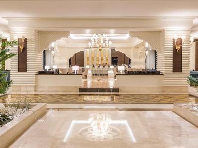 Elegante Hotellobby mit Marmorboden, Kronleuchter, Palmen und weißen Blumenarrangements.