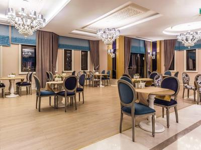 Eleganter Speisesaal mit hölzernen Tischen, blauen Sesseln und Kronleuchtern an hellem Boden.