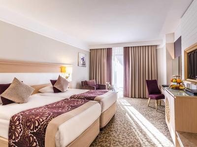 Modernes Hotelzimmer mit zwei Einzelbetten, violetten Akzenten und großer Fensterfront mit Vorhängen.