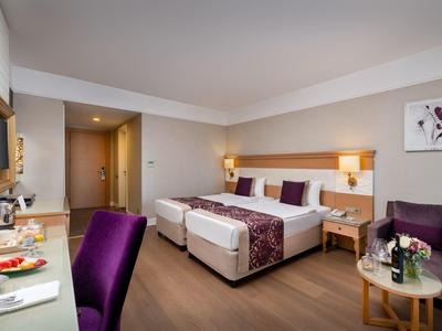 Camera d'hotel luminosa con due letti singoli, accenti viola e arredi moderni.