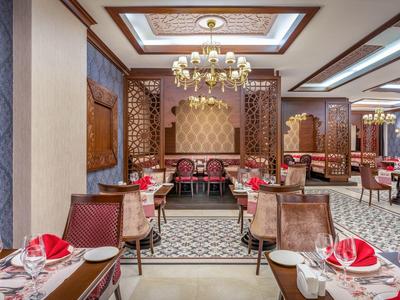 Ristorante elegante con lampadario, pareti decorate e tavoli apparecchiati con tovaglioli rossi.